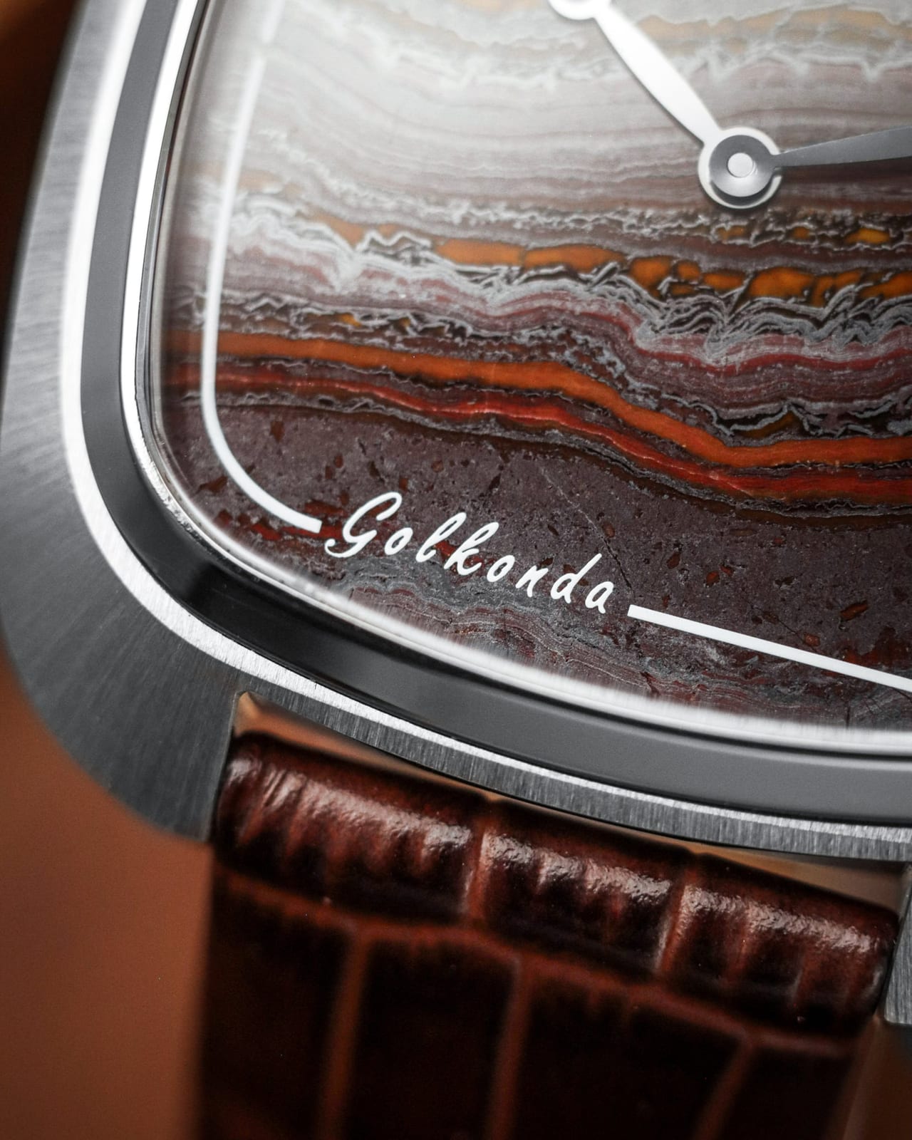 Macro photograph of the Golkonda Tiger Ferrum's natural tiger iron stone dial, with bands of gold, rust red and steel grey beneath a polished steel cushion case, signed Golkonda
