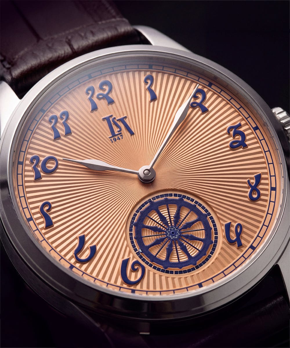 Close-up of the IST 1947 Arka Golden Hour dial: salmon sunray finish, deep blue Devanagari-inspired numerals and a blue Konark Wheel small seconds at 6 o'clock