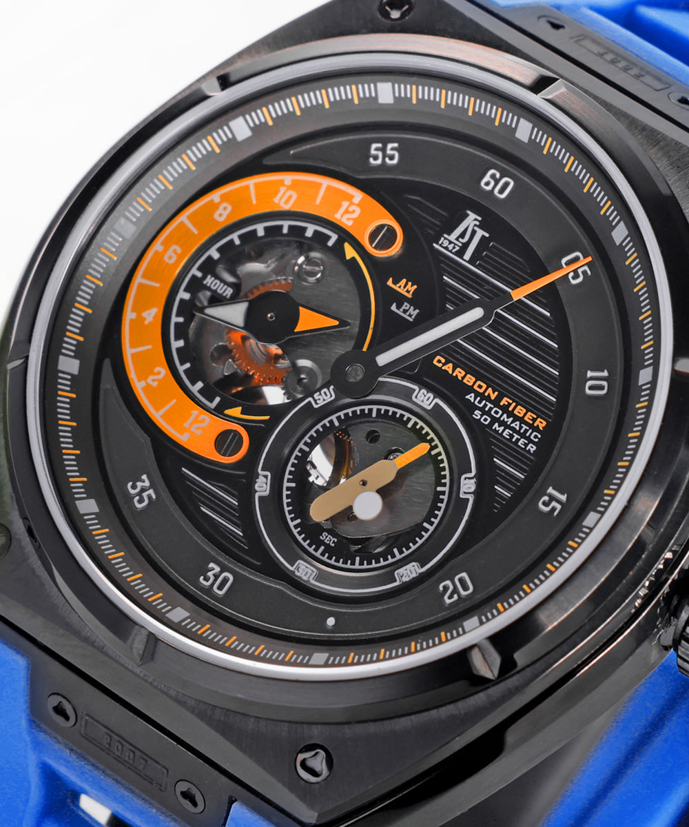 Close-up of the IST 1947 Vijay 2011 dial: carbon-fibre texture, an orange open-worked arc at 9 o'clock and a bat-and-ball small seconds at 5